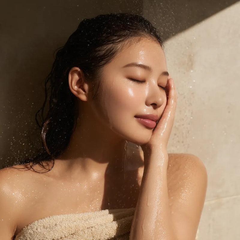 Femme apaisée éclaboussant son visage d’eau fraîche dans une ambiance spa douce, évoquant l’hydratation intense et naturelle des soins visage haut de gamme. collection